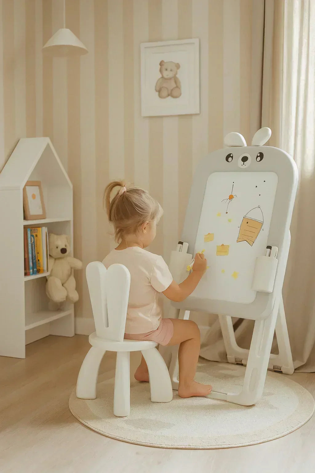 Детска стая с малко момиче на заешки стол и дъска за рисуване, играчки и книги